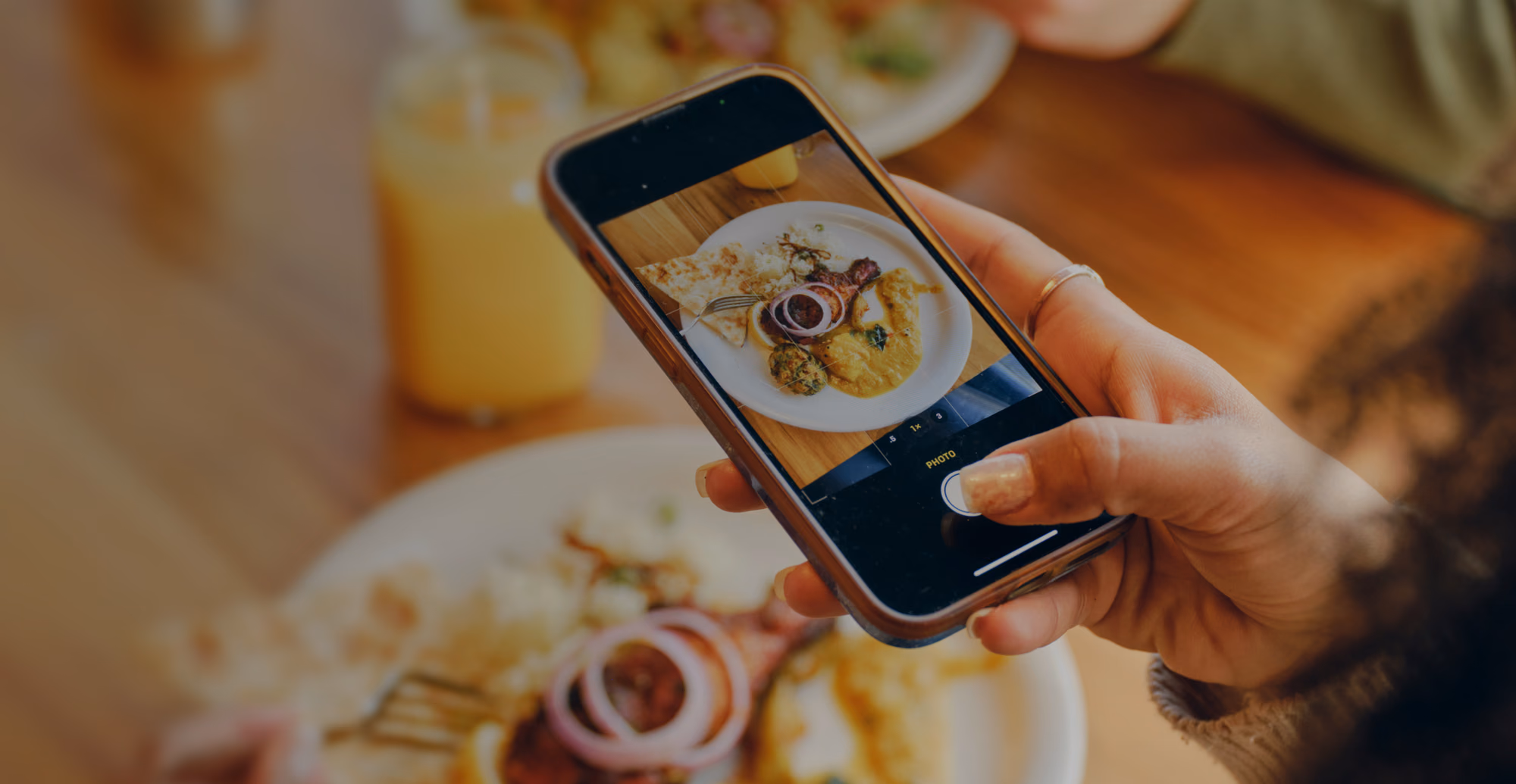 A person holding a smartphone to take a photo of a plate with curry, rice, meat, and flatbread, looking their meal on the Verily Me app