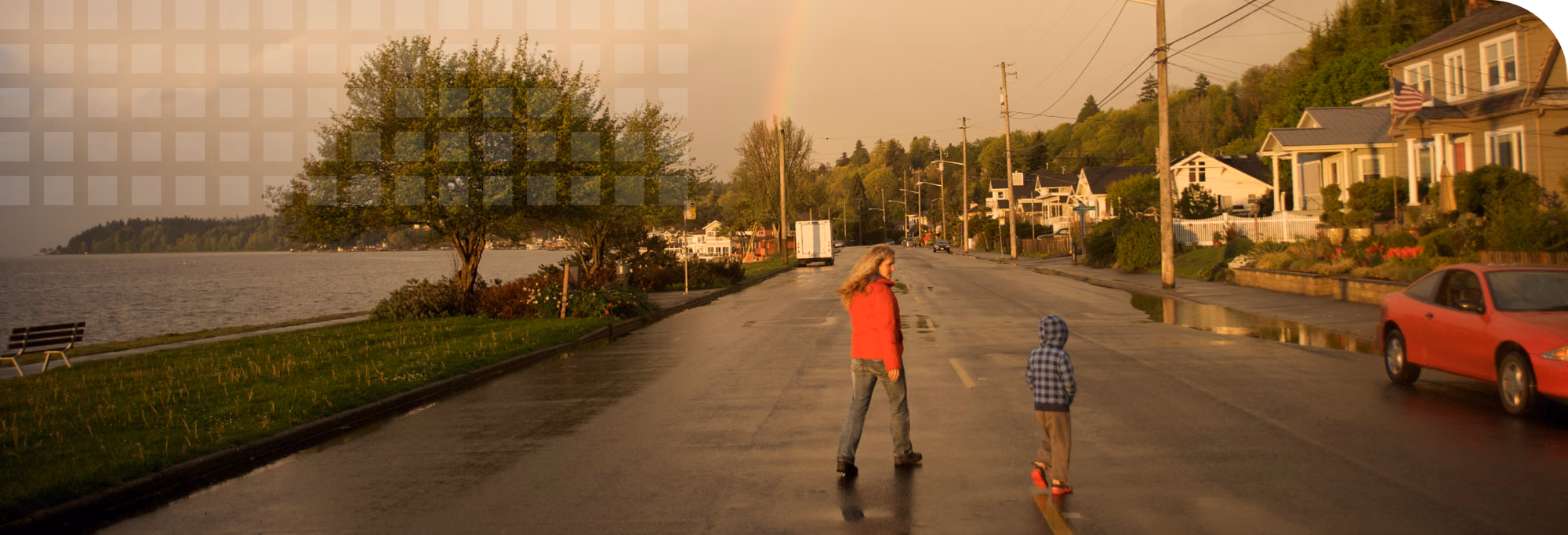Mother and son walking with zest in their community along the water on a drizzly day with a rainbow on the horizon.