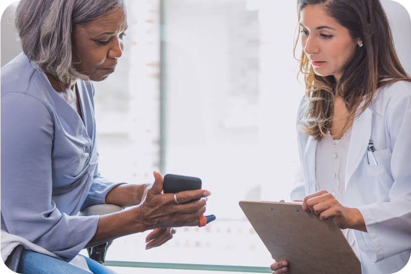 A woman shows something on her phone to a clinician with a clipboard